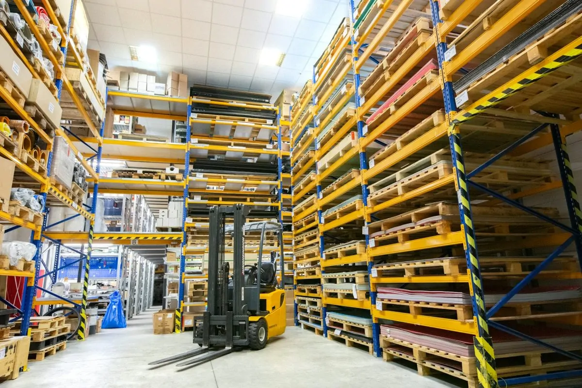 Well-organized warehouse with tall industrial storage racks, a forklift in operation, and neatly stacked pallets, representing efficient logistics and supply chain management.