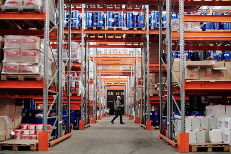 Warehouse worker inspecting stocked shelves in a large distribution center for 3PL logistics and ecommerce fulfillment.